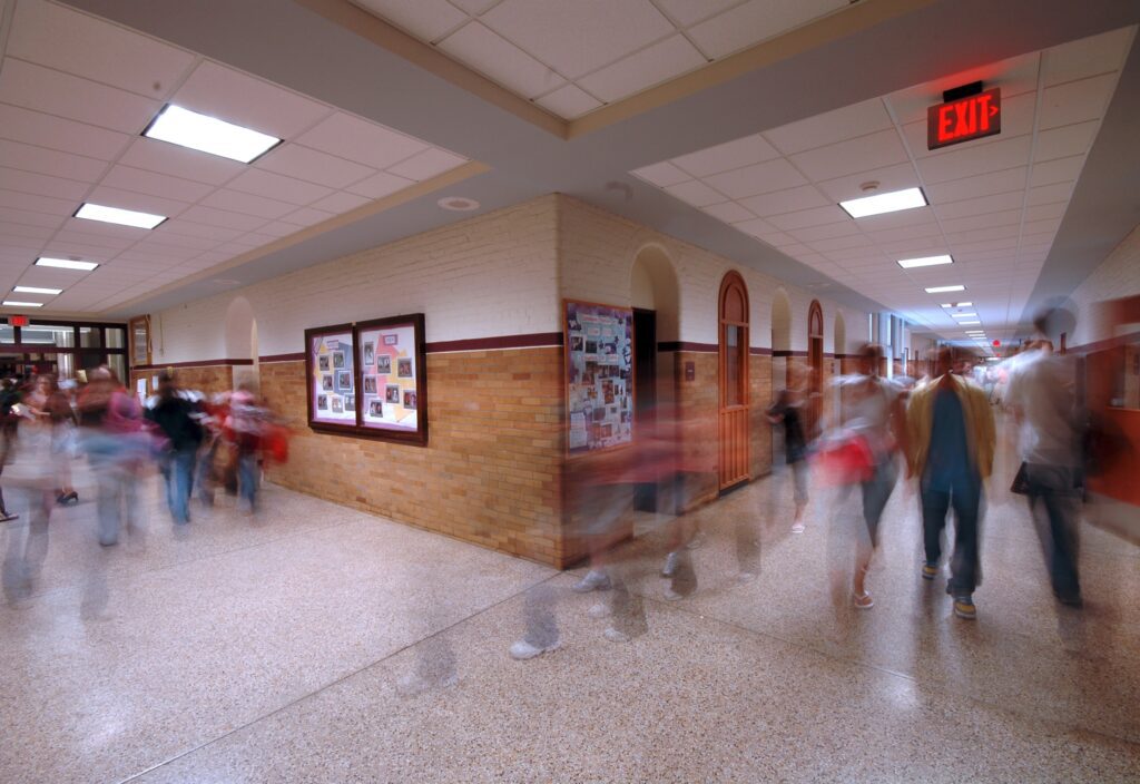 A school hallway with the rushing blurred images of children and youth moving through the halls, symbolizing the passage of time throughout the day and potentially demonstrating some type of emergency response.