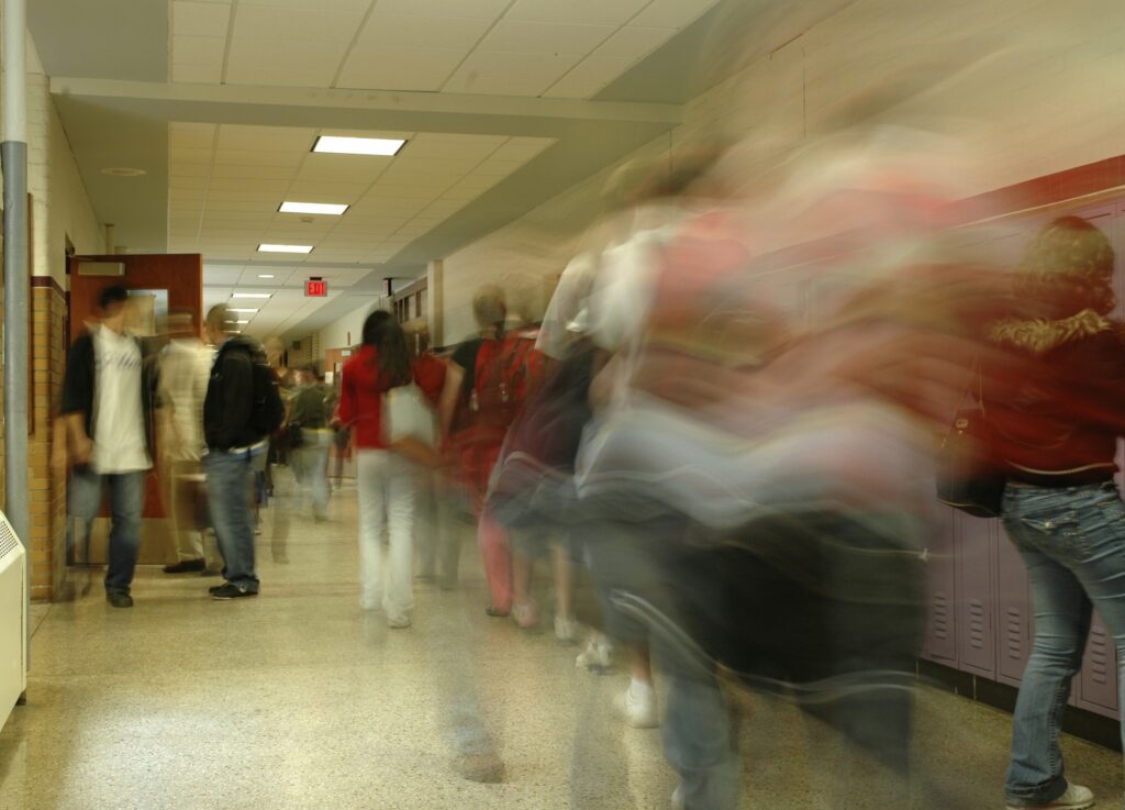 The image shows a hallway in a school full of children making their way to classes. There is a blur effect on those moving through the hallway, demonstrating the quick passage of time.